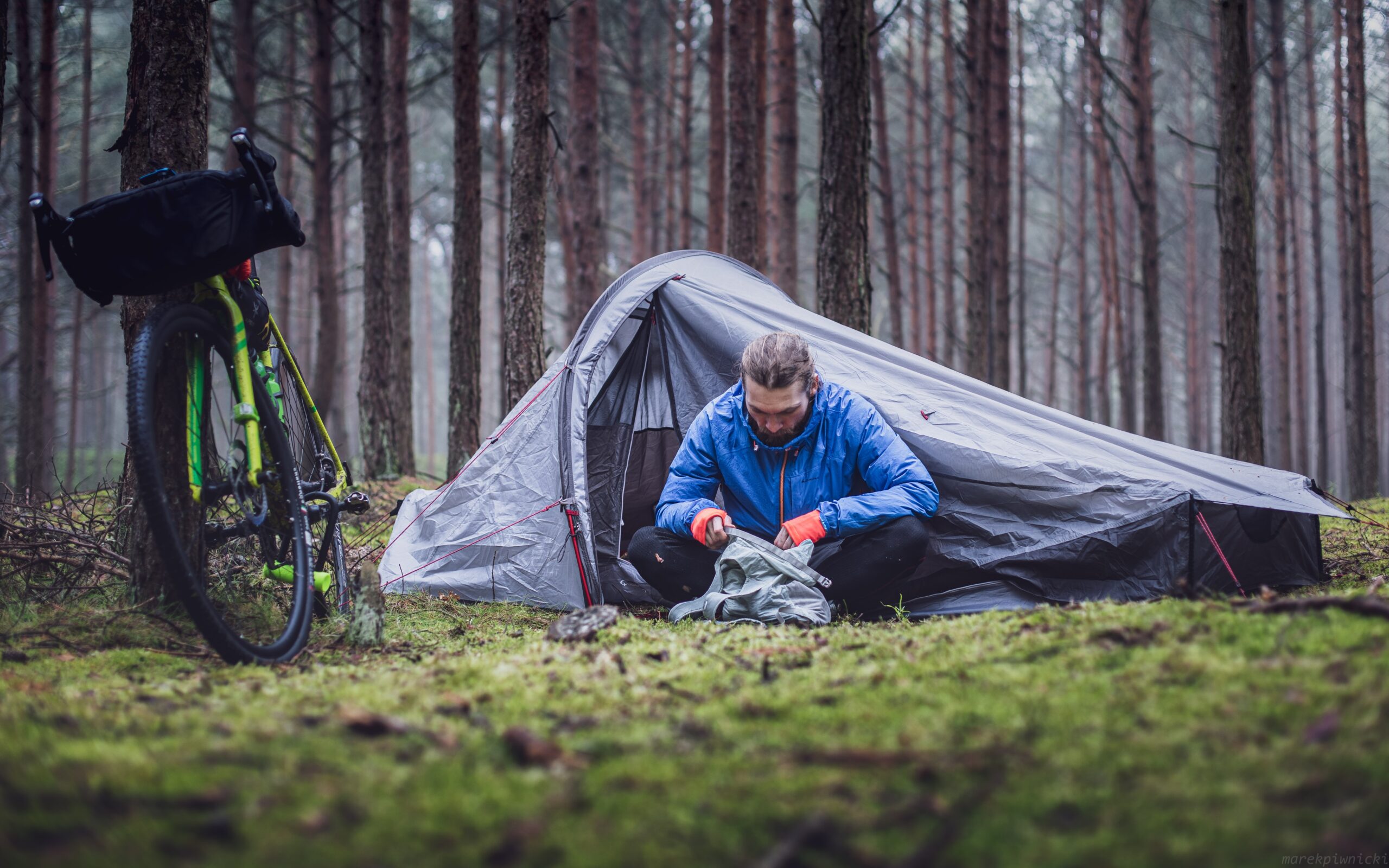 Man camping next to his bike in a forest - Photo by Marek Piwnicki on Unsplash