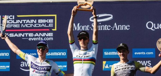 Finn Treudler celebrates at the Cube Factory Racing Season Finale 2025 in Mont-Sainte-Anne, holding the trophy aloft, flanked by the second- and third-place riders on the podium.