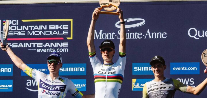 Finn Treudler celebrates at the Cube Factory Racing Season Finale 2025 in Mont-Sainte-Anne, holding the trophy aloft, flanked by the second- and third-place riders on the podium.