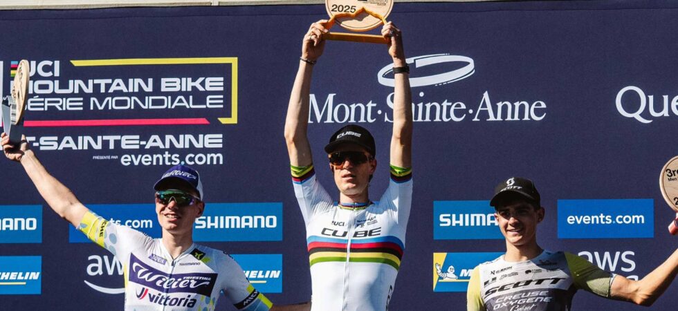 Finn Treudler celebrates at the Cube Factory Racing Season Finale 2025 in Mont-Sainte-Anne, holding the trophy aloft, flanked by the second- and third-place riders on the podium.