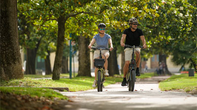 A couple rides their folding bikes through a park.